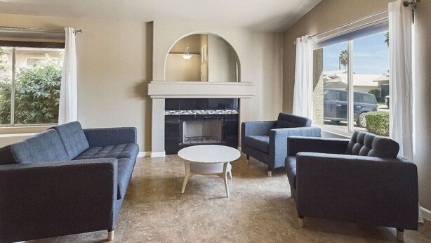 A living room with a fireplace, two sofas, a coffee table, and large windows with curtains.