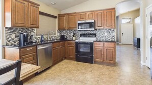 A modern kitchen with wooden cabinets, a stainless steel dishwasher, a microwave, a stove, and a tiled backsplash.