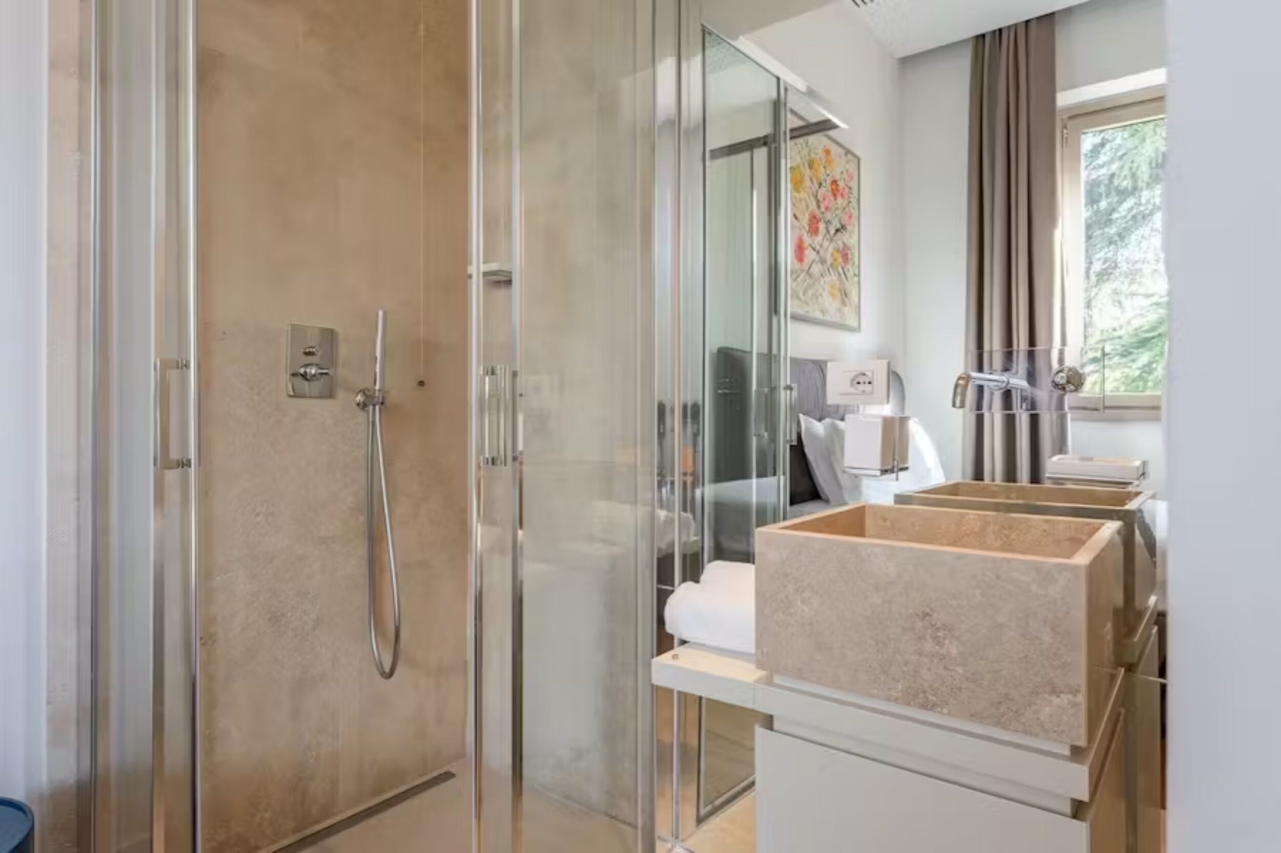 Ein modernes Badezimmer mit einer gläsernen Duschkabine, einem weißen Waschbecken mit beiger Arbeitsplatte und einem großen Fenster für natürliches Licht.
