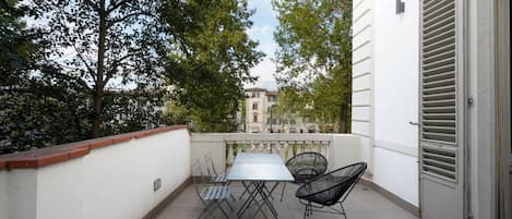 A balcony with a table and chairs, overlooking a building and trees.