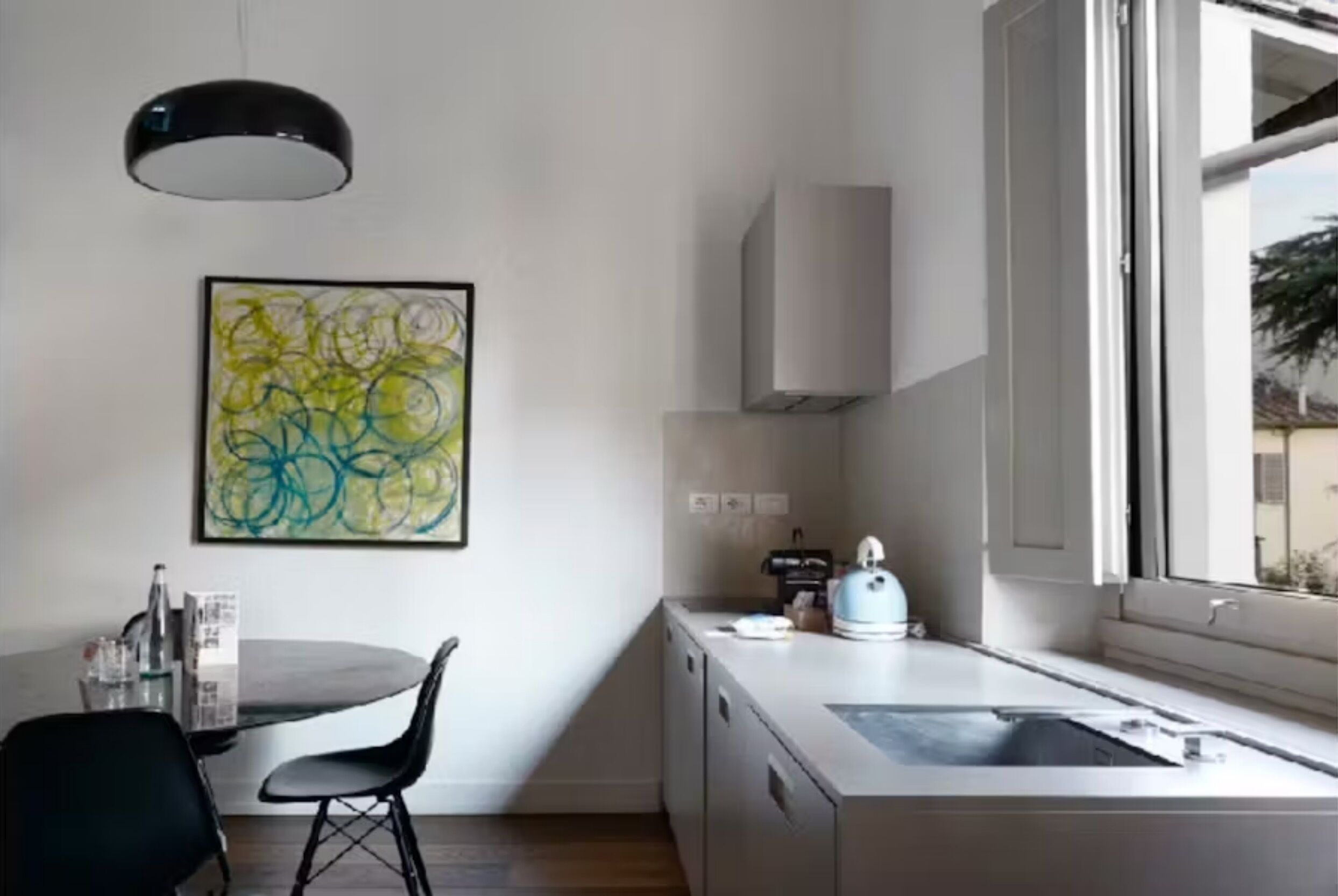 A modern kitchen with a round dining table, black chairs, a white cabinet, and a window with a view.