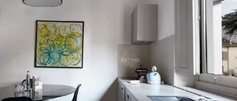 A modern kitchen with a round dining table, black chairs, a white cabinet, and a window with a view.