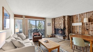 A cozy living room with a fireplace, a dining area, and a sofa. - Special VRBO Savings! Pool/HT, Balcony & Covered Parking (Snowmass Village)