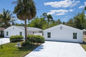 Un barrio residencial con dos casas blancas, una palmera y cielo despejado.