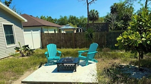 A patio with two turquoise Adirondack chairs and a small table, surrounded by a wooden fence and greenery. - Pelican Room- Cute Bungalow near Beaches Downtown (Bonita Springs)
