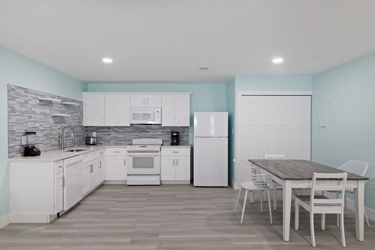 A modern kitchen with white cabinets, a microwave, a refrigerator, and a dining table with chairs.