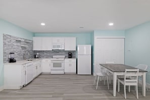 Una cocina moderna con armarios blancos, microondas, refrigerador y una mesa de comedor con sillas.
