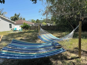 Una hamaca en un patio trasero con una casa y una valla de madera al fondo.