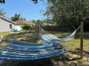 Una hamaca en un patio trasero con una casa y una valla de madera al fondo.