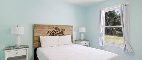 Un dormitorio con una cama, dos mesitas de noche, un ventilador de techo y una ventana con cortinas.