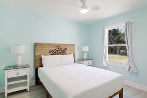 A bedroom with a bed, two bedside tables, a ceiling fan, and a window with curtains.