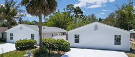 A residential area with two white houses, a palm tree, and a clear sky.