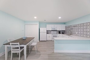 A compact kitchen with white cabinets, a dining table with chairs, and a patterned backsplash.