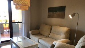 A living room with a beige sofa, a glass coffee table, a floor lamp, and a painting on the wall.