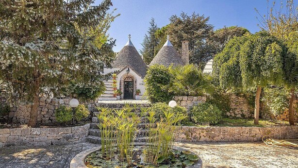 A courtyard with a stone fountain, a small bridge, and a building with conical roofs.