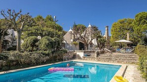 A swimming pool with a lifebuoy and a yellow float ring, surrounded by stone steps and a building with a tiled roof.