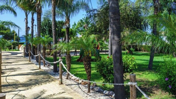 A pathway lined with palm trees and a grassy area with a playground. - Refugio de Riviera 2 bed apt with sea view (Mijas Costa)