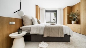 A modern bedroom with a bed, bedside table, and a potted plant. - Lomas del Marbella | Puente Romano Penthouse (Marbella)