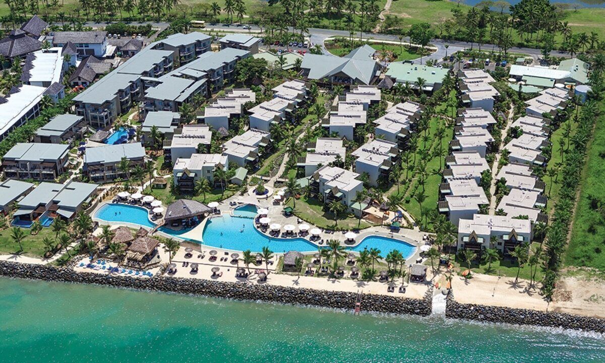 An aerial view of a resort with multiple buildings, a central swimming pool, and a beach area.