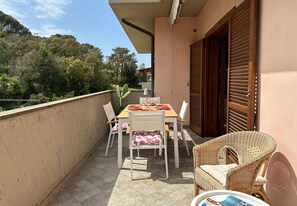 A balcony with a table set for dining, white chairs, wicker furniture, and a view of trees and hills. - La Perla di Porto Azzurro (Porto Azzurro)