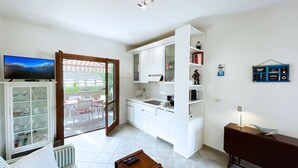 A compact living space with a kitchenette, a dining area with a table and chairs, a sofa, a wooden coffee table, and a television mounted on the wall. - La Perla di Porto Azzurro (Porto Azzurro)