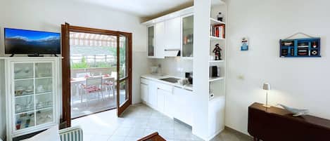 A compact living space with a kitchenette, a dining area with a table and chairs, a sofa, a wooden coffee table, and a television mounted on the wall.