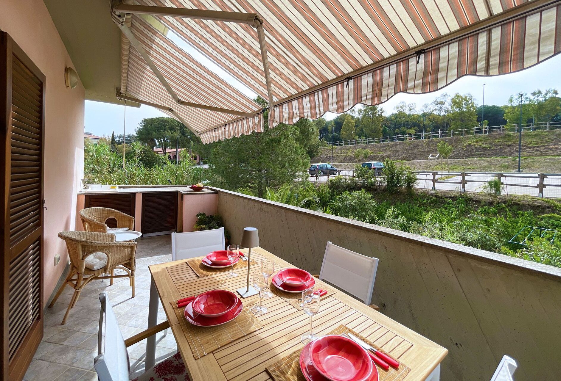 Un balcón con una mesa lista para comer, sillas y un toldo a rayas.
