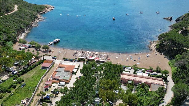 An aerial view of a coastal area with a beach, boats, and a parking lot with buildings. - La Perla di Porto Azzurro (Porto Azzurro)