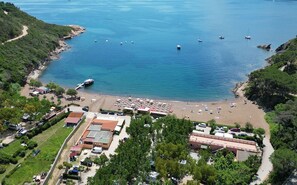 An aerial view of a coastal area with a beach, boats, and a parking lot with buildings. - La Perla di Porto Azzurro (Porto Azzurro)