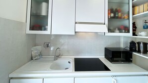 A modern kitchen with white cabinetry, a stainless steel sink, a black countertop, and a microwave. - La Perla di Porto Azzurro (Porto Azzurro)
