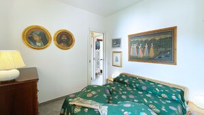 A bedroom with a bed, a lamp, two framed portraits, and a painting on the wall. - La Perla di Porto Azzurro (Porto Azzurro)