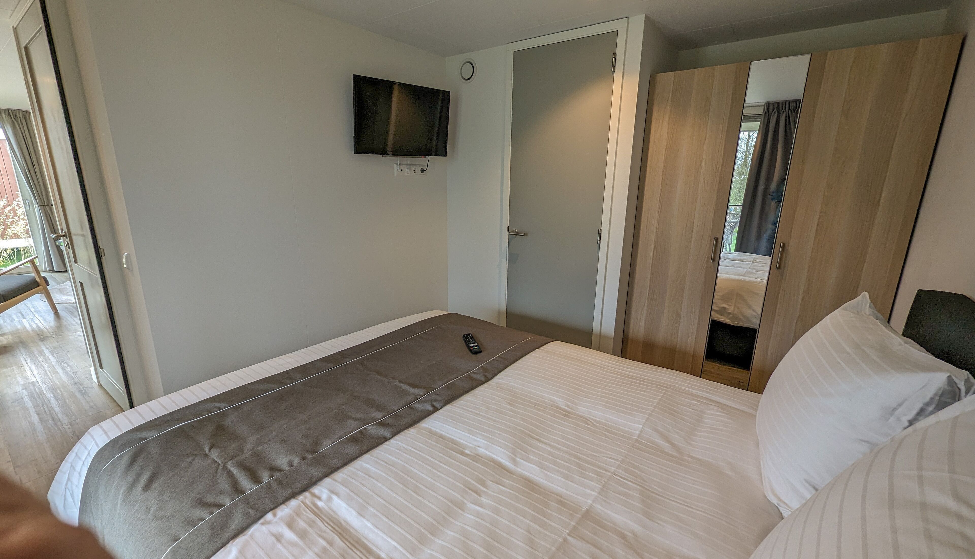 A bedroom with a bed, a TV mounted on the wall, and a wardrobe.