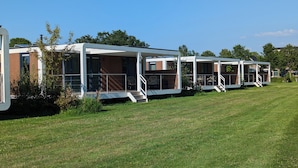 A row of modern mobile homes with outdoor patios, each featuring a small staircase leading to a deck. - Antonius Hoeve Chalets (Oudenbosch)