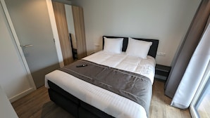 A neatly made bed with a remote control on it, a bedside table, and a wardrobe with a mirror. - Antonius Hoeve Chalets (Oudenbosch)