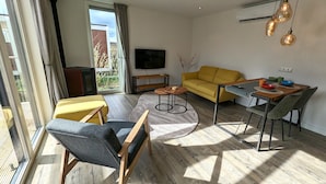 A modern living room with a yellow sofa, a wooden coffee table, and a TV mounted on the wall. - Antonius Hoeve Chalets (Oudenbosch)