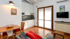 Een ruimtelijk ingerichte leefruimte met een kitchenette, een eethoek, een bank en een televisie.