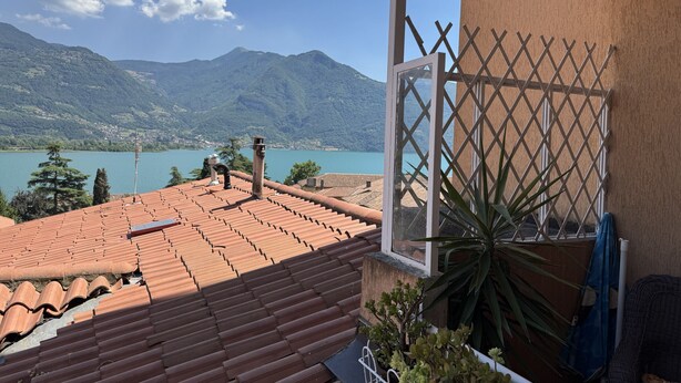 Un balcon avec des carreaux de terre cuite, une vue sur un lac, des montagnes et une fenêtre à croisillons.