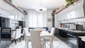 Une cuisine moderne avec des meubles blancs, un coin repas comprenant une table et des chaises blanches, et un canapé bleu.
