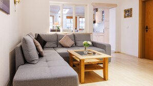 A living room with a grey sectional sofa, a wooden coffee table, and a view into the kitchen. - Ferienwohnung Unternberg 45qm, Terr., Küche, Behinderteng., 1 Schlafzimmer (Ruhpolding)