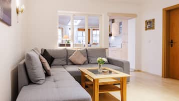 Ein Wohnzimmer mit grauem Ecksofa, einem Holztisch und Blick in die Küche.
