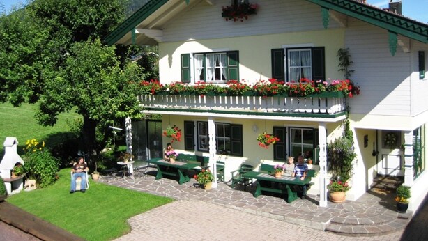 A two-story building with a balcony, outdoor seating, and a stone-paved patio. - Ferienwohnung Unternberg 45qm, Terr., Küche, Behinderteng., 1 Schlafzimmer (Ruhpolding)