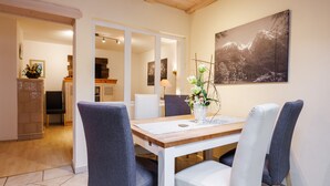 A dining area with a wooden table, four chairs, and a vase with flowers. - Ferienwohnung Unternberg 45qm, Terr., Küche, Behinderteng., 1 Schlafzimmer (Ruhpolding)