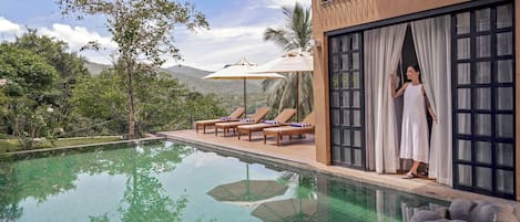A poolside area with lounge chairs, a view of the surrounding landscape, and a building with large windows.