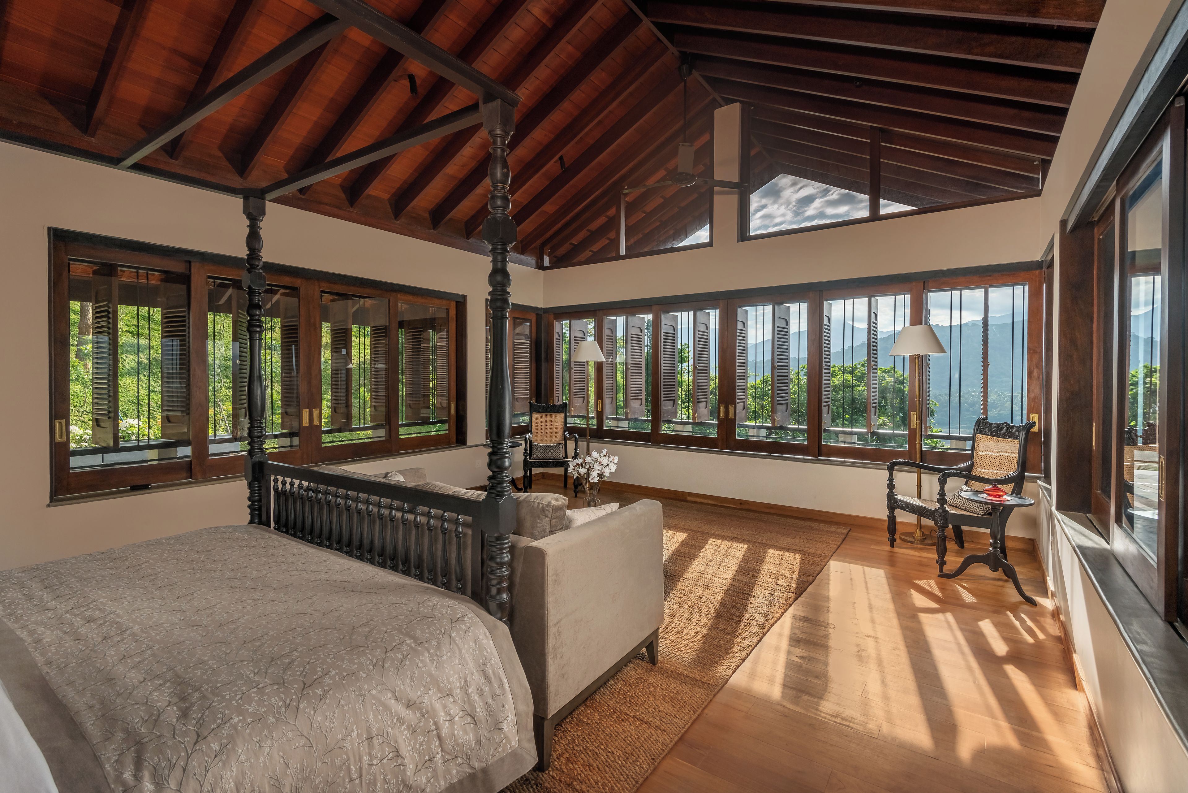 A spacious bedroom with a four-poster bed, large windows, and a view of the outdoors.