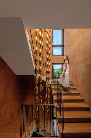 Una escalera con un adorno dorado único, vistas de vegetación al exterior y una persona con un vestido blanco.