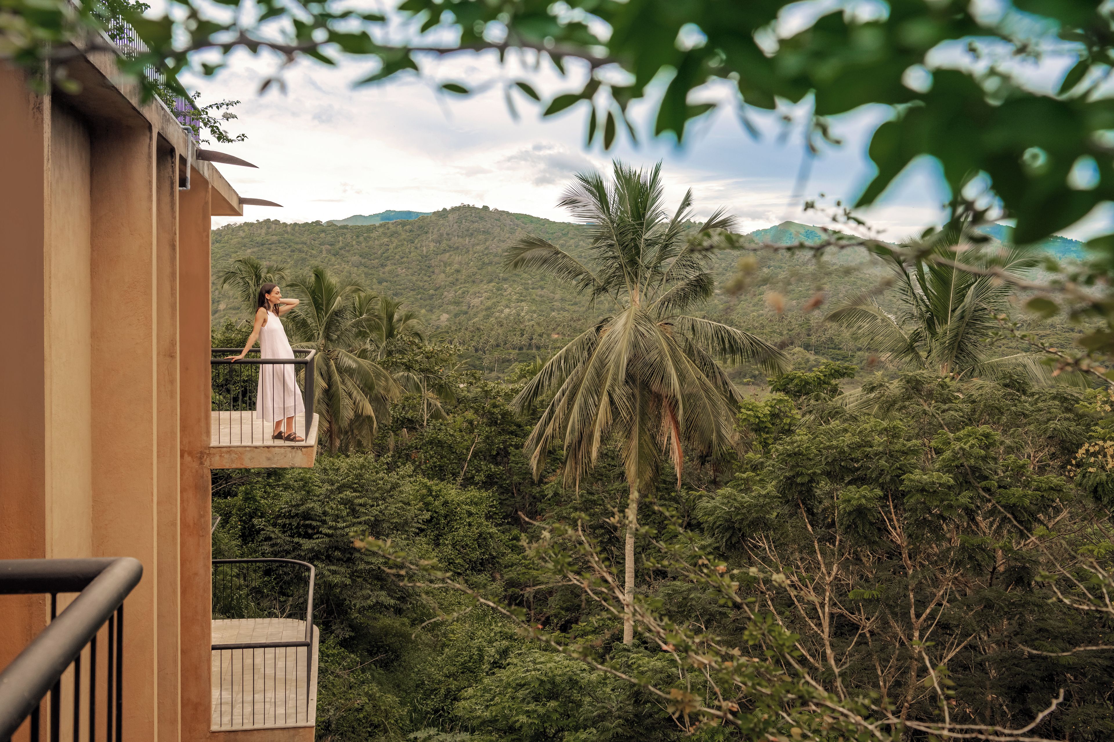 A balcony with a view of a lush green landscape, including palm trees and a mountain in the distance.