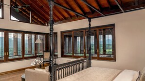 A bedroom with a four-poster bed, large windows with shutters, and a view of the outdoors.