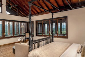 Un dormitorio con cama con dosel, ventanas amplias con contraventanas, ventilador de techo y vistas al exterior.