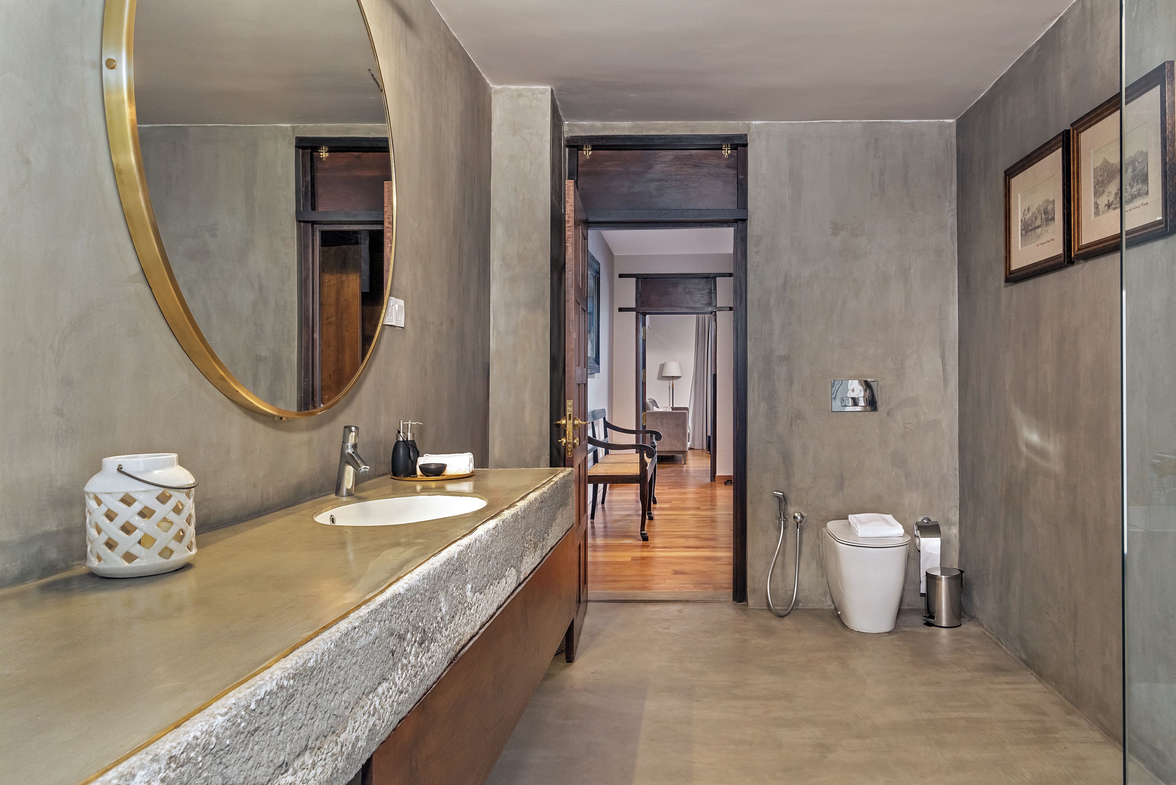 A modern bathroom with a large mirror, two sinks, a toilet, and a bench.