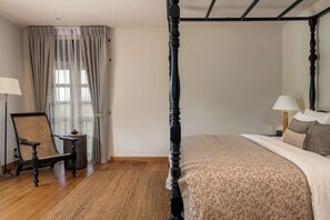 Un dormitorio con una cama con dosel, una silla, una mesita y una ventana con cortinas.